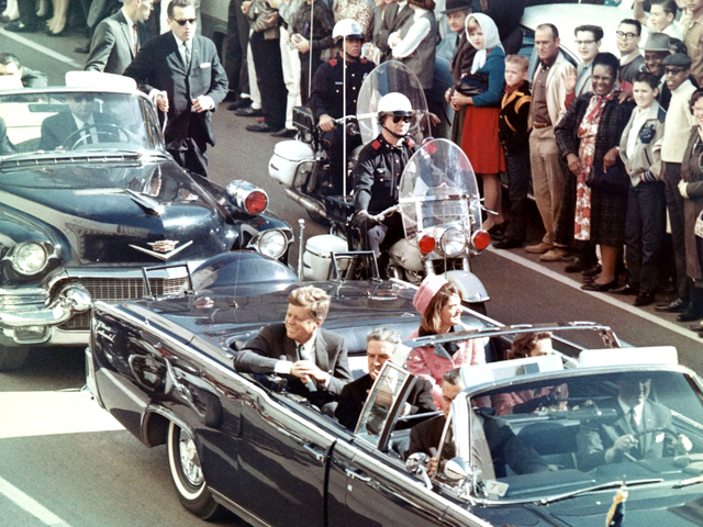 John Kennedy vẫy tay tươi cười với công chúng. Ông không hề biết rằng ở phía trước đang bị phục kích và đây cũng là ngày định mệnh của cuộc đời.