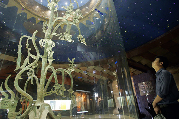Hình ảnh du khách đang xem một di tích văn hóa cây đồng được trưng bày tại Bảo tàng Tam Tinh Đôi, thành phố Quảng Hán, tỉnh Tứ Xuyên vào ngày 28/5/2005. Tạo hình của các di tích văn hoá khác nhiều với văn hóa Trung Nguyên (Liu Jin / AFP qua Getty Images)